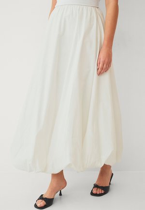 White, voluminous long skirt made of textured fabric, featuring an elastic waistband. Paired with black high-heeled sandals.