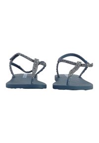 Chanclas azules con una suela texturizada, con correas plateadas brillantes y un diseño distintivo de cruce. Suela plana para mayor comodidad.