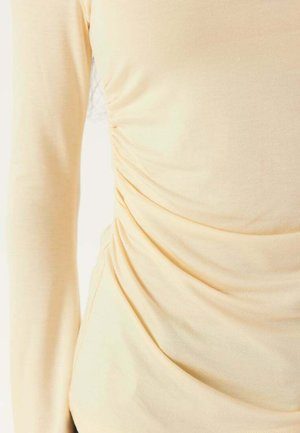 Cremefarvet langærmet skjorte med rynkedetaljer i siden og glat stoftekstur.