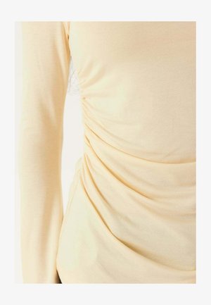 Cremefarvet langærmet skjorte med rynkedetaljer i siden og glat stoftekstur.