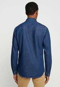 Denimhemd, dunkelblau, lange Ärmel, mit geknöpften Manschetten, spitzem Kragen und abgerundetem Saum. Sichtbare Nähte und taillierte Passform.