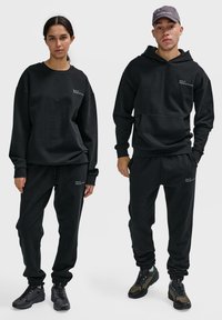Schwarzer Baumwoll-Sweatshirt und Jogginghose, mit lässiger Passform, gerippten Bündchen und minimaler weißer Markenkennzeichnung. Enthält eine Kapuze und Sneaker.