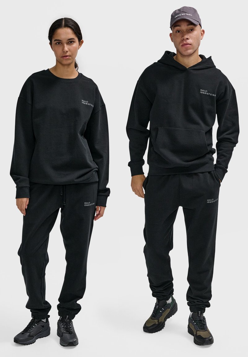 Schwarzer Baumwoll-Sweatshirt und Jogginghose, mit lässiger Passform, gerippten Bündchen und minimaler weißer Markenkennzeichnung. Enthält eine Kapuze und Sneaker.