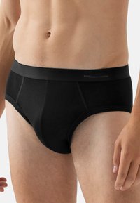 Slip in cotone nero con vita liscia, dotato di una tasca frontale e dettagli cuciti ai lati. Vestibilità regolabile. Design casual.