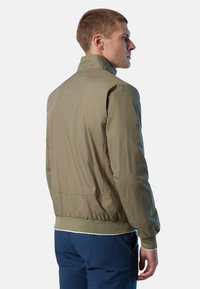 Giacca leggera verde oliva con colletto rialzato, polsini elasticizzati e orlo. Tessuto liscio e lucido con un design semplice e senza motivi visibili.