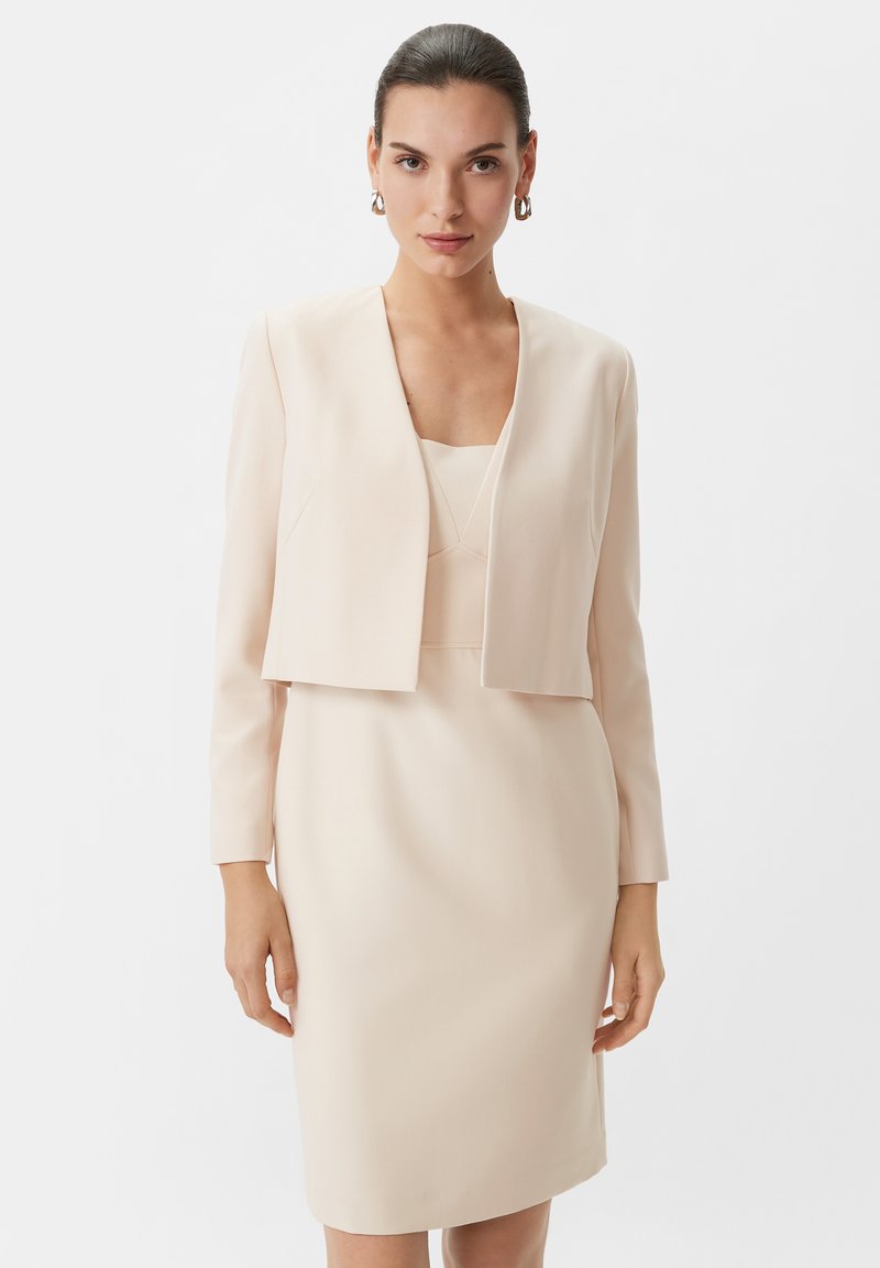 Helles rosa Anzug mit einer taillierten Jacke mit langen Ärmeln und einem passenden knielangen Kleid. Glattes Material mit minimalen Details.