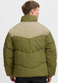 Chaqueta de plumas verde oliva con sección de hombro beige en contraste, textura acolchada, cuello alto y detalle de costura en forma de Chevron.