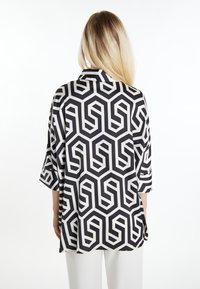Bluză cu model alb-negru, cu un design geometric, mâneci trei sferturi și croială lejeră, cu guler. Textură netedă.
