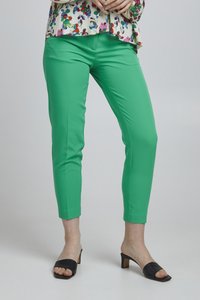 Groene enkel-lange broek van een gladde stof, met een strakke pasvorm. Gecombineerd met zwarte open teen hakken voor een eigentijdse look.