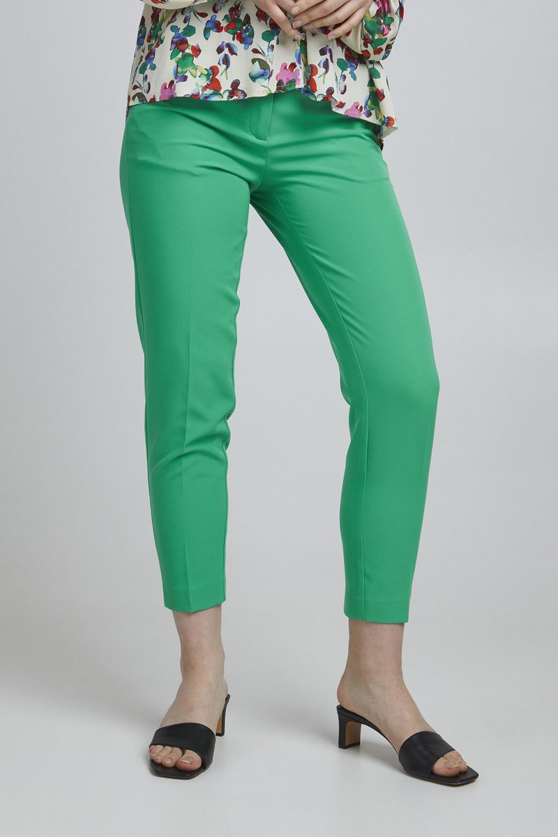 Groene enkel-lange broek van een gladde stof, met een strakke pasvorm. Gecombineerd met zwarte open teen hakken voor een eigentijdse look.