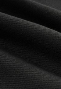 Nahaufnahme von schwarzem ribbeligem Stoff mit sichtbarem diagonalen Strickmuster und weichen Falten.