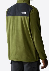 Zielona polarowa kurtka z czarnym panelem na ramieniu i logo. Miękka tekstura, pełny zamek błyskawiczny oraz długie rękawy. Dolny brzeg prosty i swobodny krój.