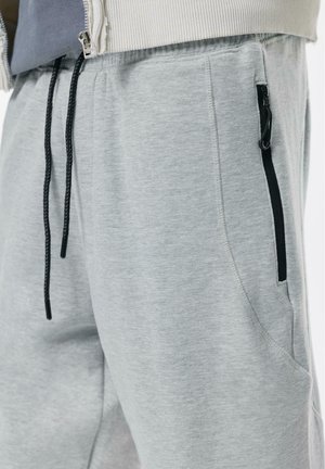 Pantaloni de trening gri dintr-un amestec moale de bumbac, cu un design conic, talie elastică cu șnur și buzunare laterale cu fermoar.