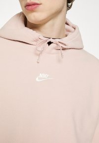 Felpa con cappuccio in pile rosa con coulisse sul cappuccio e logo Nike bianco sul petto. Tessuto morbido con vestibilità rilassata.