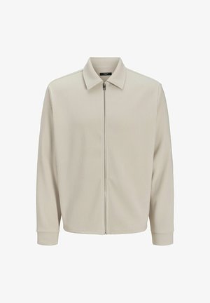 Beige gerippte Jacke mit Kragen, Reißverschluss auf der Vorderseite und langen Ärmeln. Das Material hat eine strukturierte Textur und eine klare Silhouette, die sich gut zum Schichten eignet.