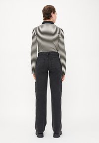 Pantaloni cargo neri a vita alta con tasche laterali, realizzati in denim. Abbinati a una maglietta a maniche lunghe a righe con colletto nero.