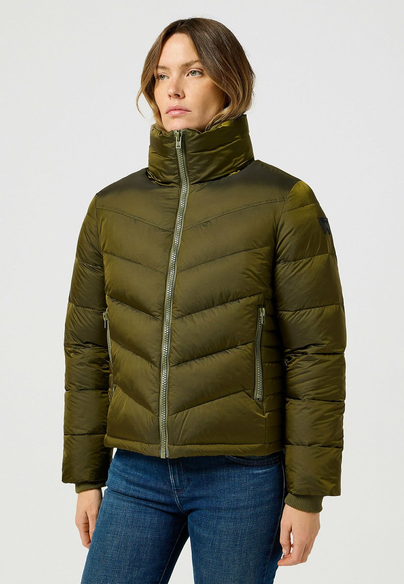 Oliwkowa, ocieplana kurtka puff z wysokim kołnierzem, w chevronowe przeszycia i dwoma zamykanymi na zamek bocznymi kieszeniami, cechująca się smukłym designem.