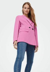 Blazer rosa a righe con un design doppiopetto, rever a punta e tasche, abbinato a jeans skinny blu. Texture liscia.