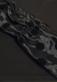 Tessuto nero a pois con una texture lucida, caratterizzato da aree arricciate e uno sfondo opaco contrastante. Motivi circolari su tutta la superficie.