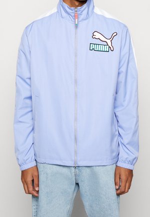 Lichtblauw jack met rits, gemaakt van gladde stof, met witte accenten op de schouders en een Puma-logo op de borst. Elastische boorden aan de mouwen.