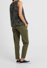 Top senza maniche con stampa floreale nera e dettagli in verde, rosso e blu; abbinato a pantaloni affusolati verde oliva e sneakers nere.
