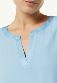 Himmelblaues Oberteil mit einem runden Ausschnitt und einem kleinen Schlitz. Der Stoff ist glatt mit einem leichten Glanz und einer sauberen Verarbeitung an den Kanten.
