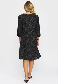 Svart och vit prickig knä-lång klänning med trekvartsärmar, en utsvängd kjol och en detalj med bakstängning. Slät struktur.