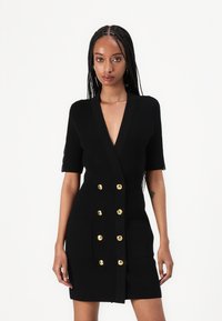Μαύρο εφαρμοστό φόρεμα από ριμπ ύφασμα, με κοντά μανίκια, βαθύ V-λαιμόκοψη, διπλό μπροστινό κούμπωμα με χρυσά κουμπιά και δύο μπροστινές τσέπες.