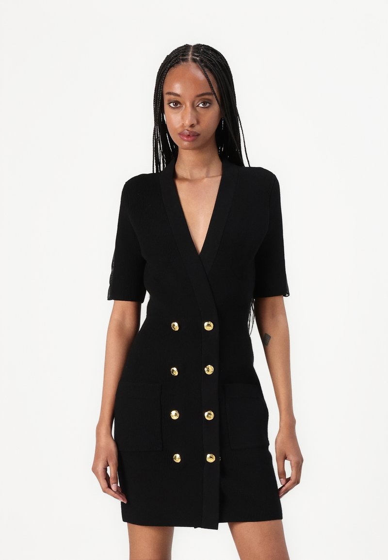 Μαύρο εφαρμοστό φόρεμα από ριμπ ύφασμα, με κοντά μανίκια, βαθύ V-λαιμόκοψη, διπλό μπροστινό κούμπωμα με χρυσά κουμπιά και δύο μπροστινές τσέπες.