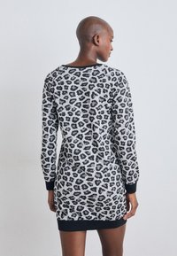 Vestido de suéter em estampado de leopardos em cinza e preto, com mangas longas, punhos canelados e um decote arredondado, destacando uma textura de malha confortável.