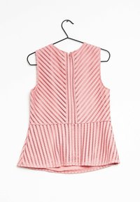 Rosa ærmeløs top med et tekstureret mønster af diagonale striber, med lynlås bagpå og en udvidet nederkant. Hænger på en sort krog.