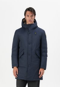Parka blu navy con cappuccio, dotata di chiusura con zip e bottoni, due tasche laterali e fodera trapuntata visibile nel colletto.