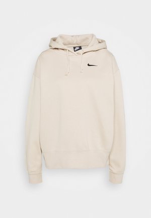 Beige Nike -huppari, jossa edessä kengurutasku, rintakehällä musta swoosh-logo, kiristysnauhallinen huppu sekä resorit hihansuissa ja helmassa.