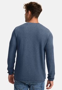 Sininen pitkähihainen neulepaita, jossa on teksturoitu neulekuvio, pyöreä pääntie ja ribattuja hihoja. Denim-housujen kanssa yhdistettynä tyyli on rento ja mukava.