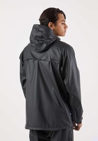 Czarna kurtka przeciwdeszczowa wykonana z wodoodpornego materiału, wyposażona w kaptur, długie rękawy oraz zatrzaski z tyłu. Gładka faktura.