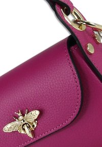 Magenta leren handtas met een gestructureerde afwerking, voorzien van een gouden bijencharme en metalen hardware op de schouderband en sluiting.