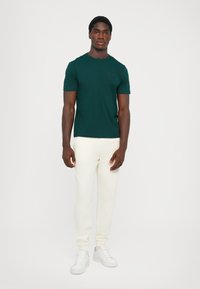 Dark green short-sleeve t-shirt with a round neckline and subtle logo. Paired with cream-colored joggers and white sneakers. Simple design.