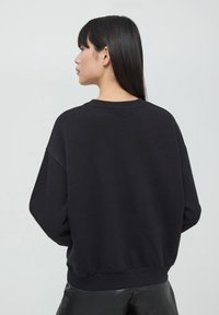 Felpa nera con vestibilità comoda, maniche larghe e orlo a coste. Materiale liscio e morbido senza pattern o loghi visibili sul retro.