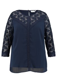 Blouse marine à manches 3/4 en dentelle, motif floral sur la dentelle, décolleté festonné et fermeture par œillet dans le dos. Tissu lisse contrastant au niveau du torse.