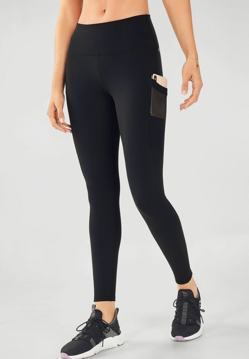 Black leggings made of stretchy material with a high waistband and a side pocket. They have a smooth texture and are fitted from waist to ankle.