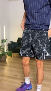 Melnas sporta šorti ar grieztu pelēku rakstu, elastīgu jostasvietu un baltiem sānu akcentiem. Kombinēti ar violetiem sporta apaviem.