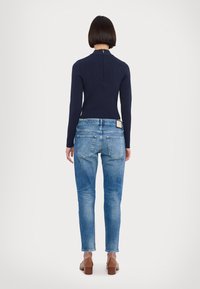 Pull en maille côtelée bleu marine avec col montant et fermeture éclair au dos, associé à un jean léger bleu clair à coupe ajustée avec un design à cinq poches et des coutures contrastantes.
