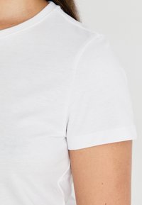 Hvit bomulls T-skjorte med rund hals og korte ermer. Stoffet ser mykt ut med en jevn tekstur og ingen synlige mønstre.