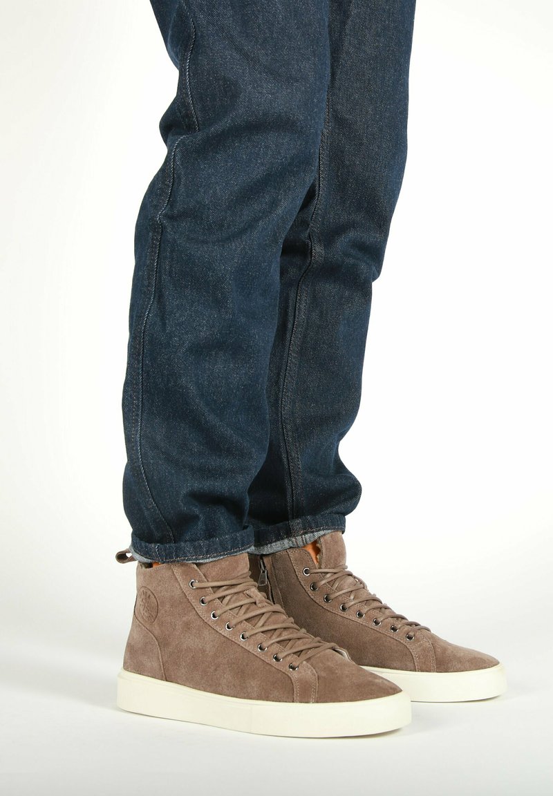 Høje suedestøvler i lys brun med hvide gummisåler, udstyret med metaløjer og snørebånd, kombineret med mørkeblå denimjeans.