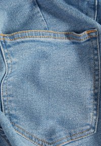 Ljusblå denimtyg med en framträdande bakficka, kontrasterande gul sömnad och en slät textur.