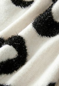 Crni plišasti točkasti uzorak na bijelom, teksturiranom materijalu stvara zanimljiv dizajn. Materijal izgleda mekano, s blagim sjajem na točkicama.