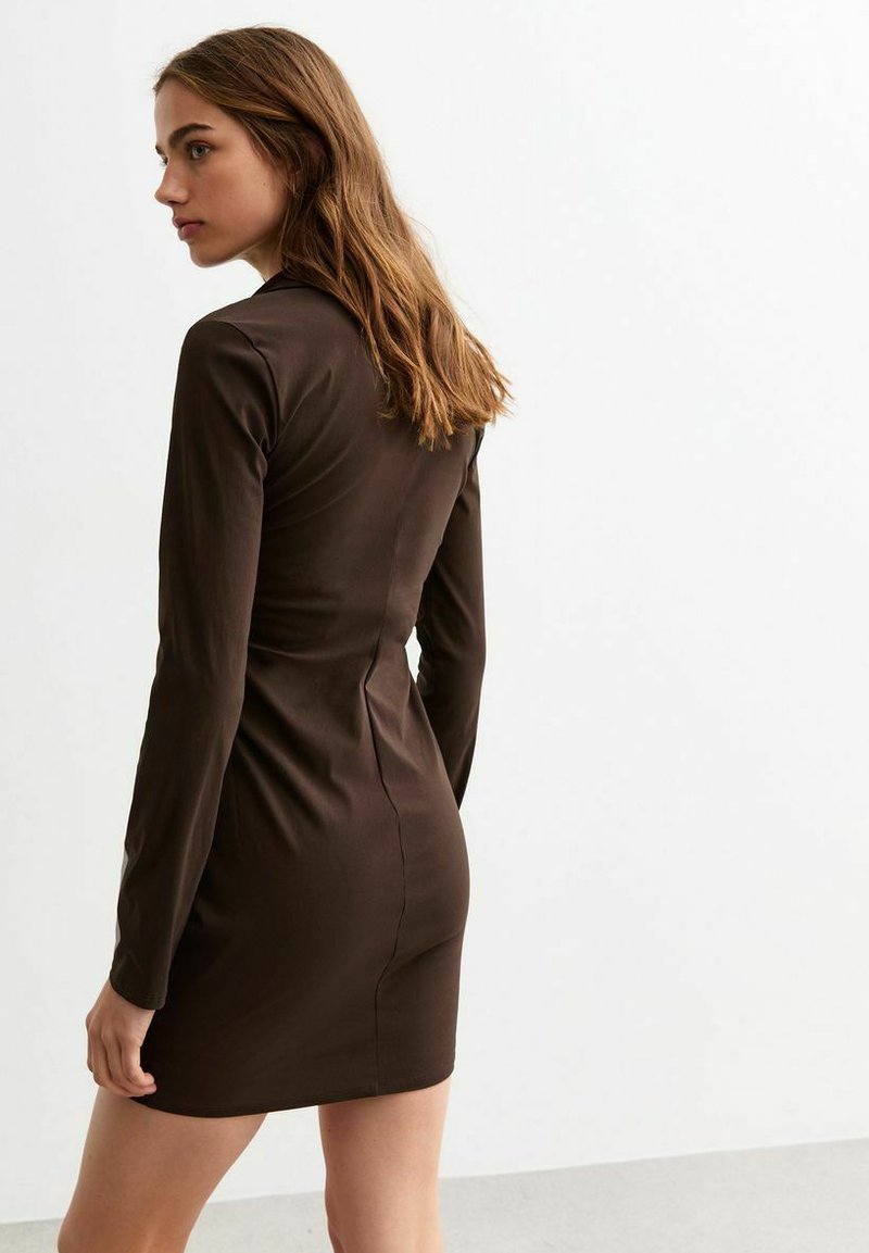Brązowa dopasowana sukienka z długimi rękawami, bezszwowym fasonem i miękką teksturą. Długość do połowy uda, lekko zwężająca się w talii, minimalistyczny styl.