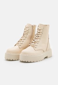 Bottines en cuir beige avec une finition texturée, des lacets et une fermeture éclair latérale. Semelle épaisse avec un motif strié.