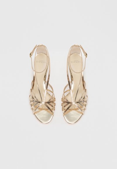 Strappy high-heeled sandals in metallic gold, featuring crossed straps, an ankle buckle, and a smooth open toe design.