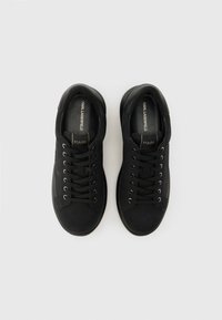 Ζευγάρι μαύρα χαμηλά sneakers Karl Lagerfeld με κορδόνια, μεταλλικά οφθαλμοθυλάκια και επενδύσεις με λογότυπο, σε ανοιχτό γκρι φόντο.